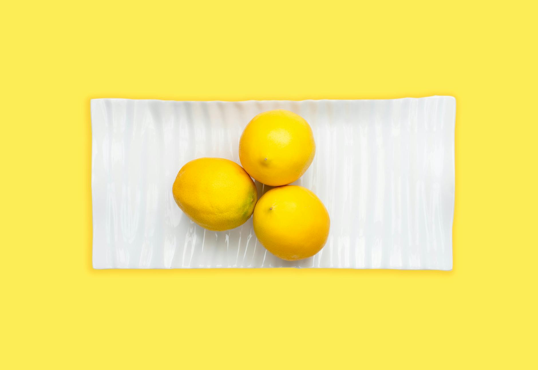 Hand holding a fresh lemon against a bright yellow background, evoking renewal and sensation