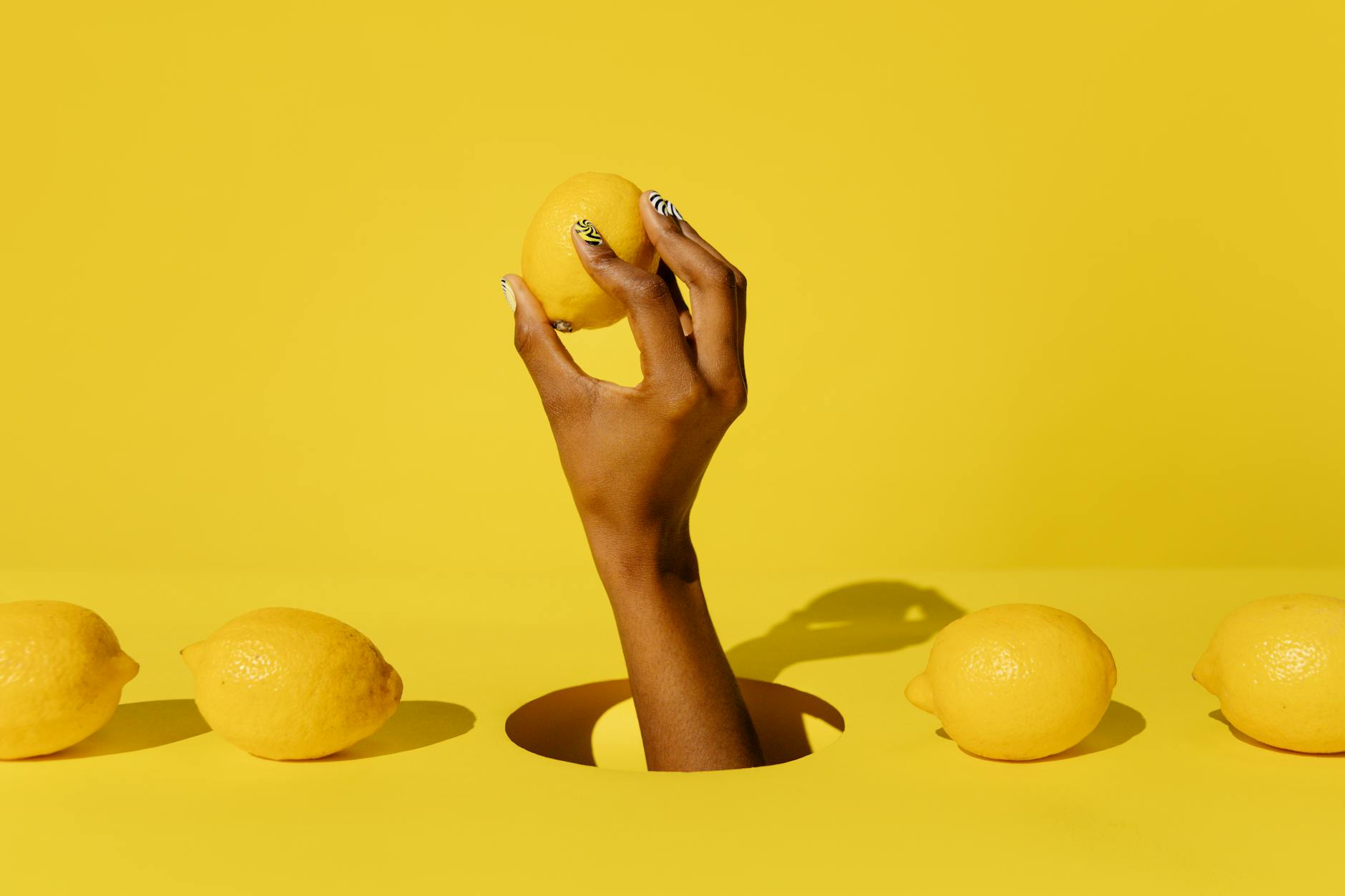 A hand holding a bright yellow lemon against a vivid yellow background, symbolizing fresh beginnings and solo pleasure