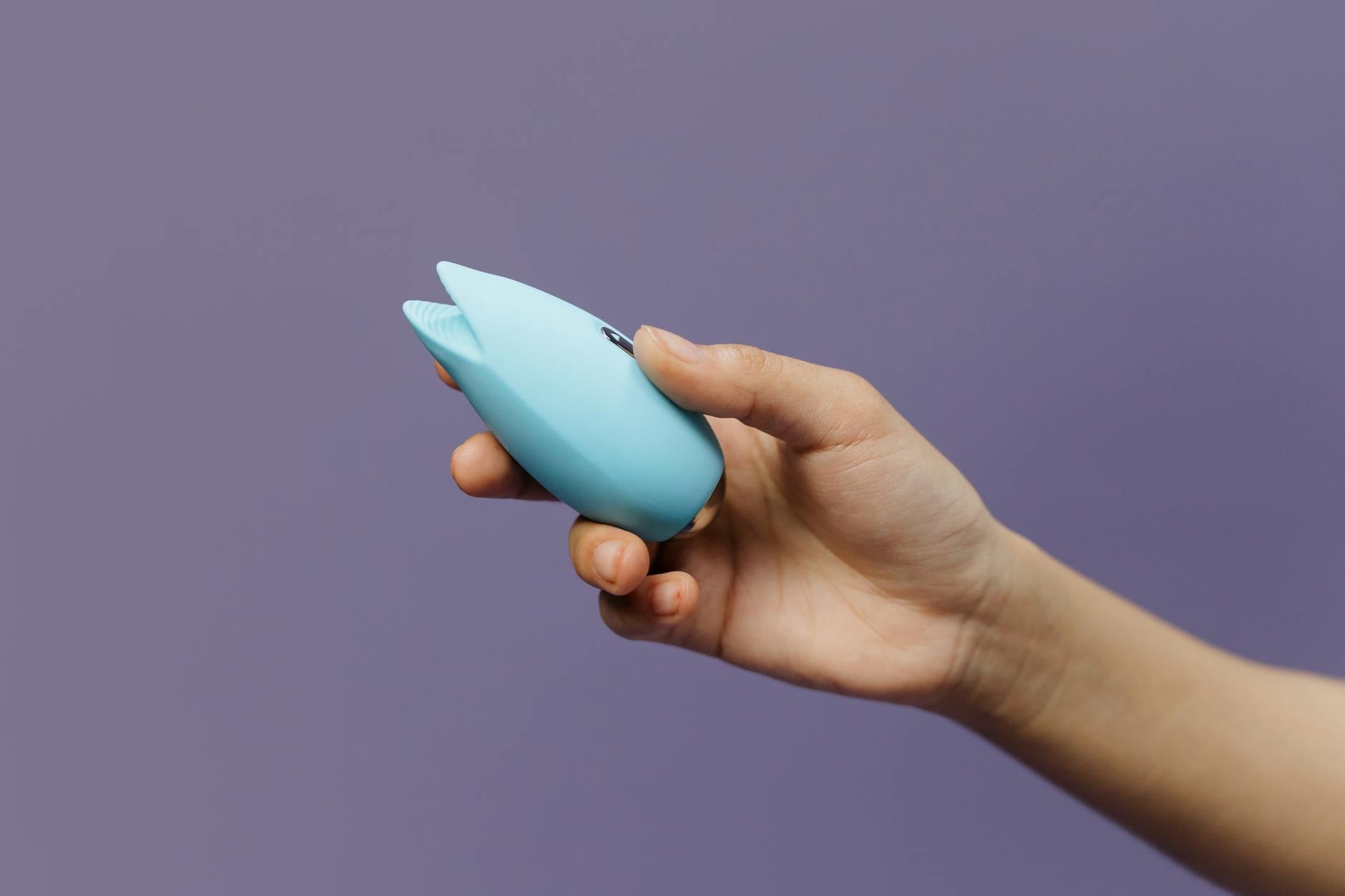 A clitoral vibrator held in hand against a solid background, promoting self-love and pleasure recovery