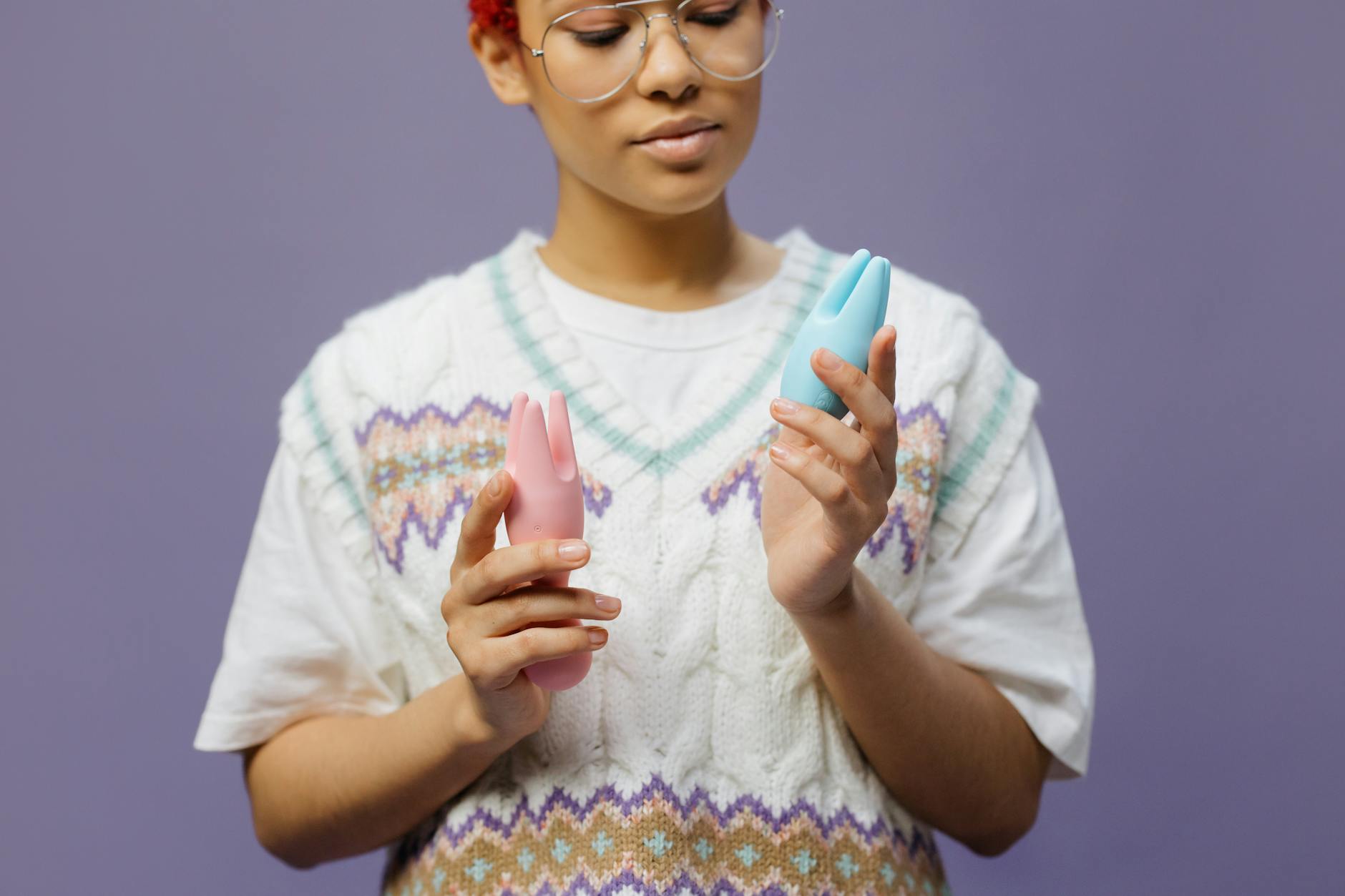 Woman holding blue and pink silicone vibrators, considering which is best for sensitive tissue.