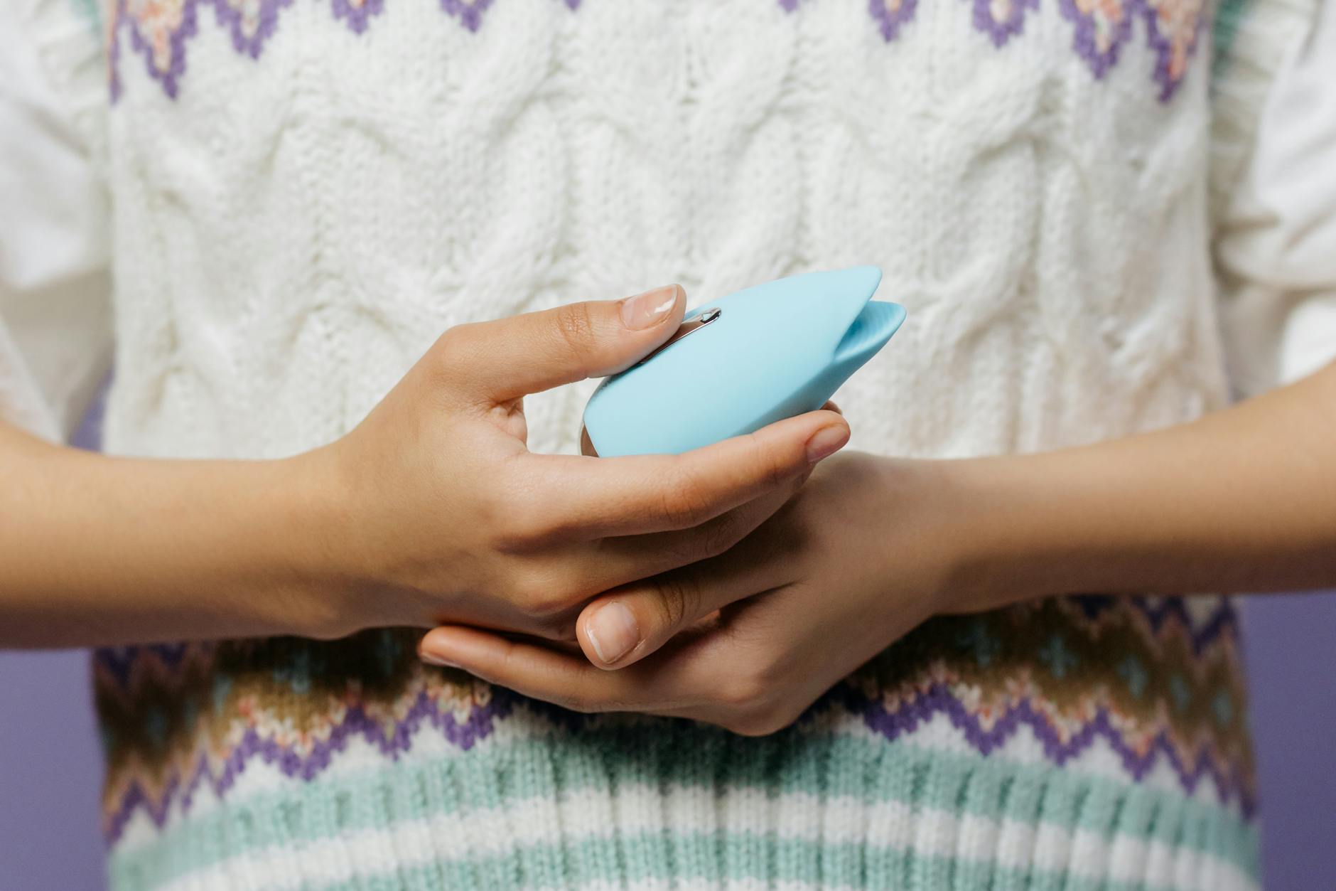 Mulher usando óculos segurando vibrador azul e rosa com expressão reflexiva