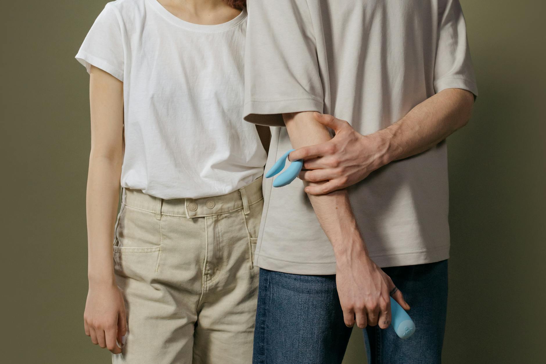 Casal jovem em pé juntos, segurando um vibrador azul, simbolizando intimidade moderna
