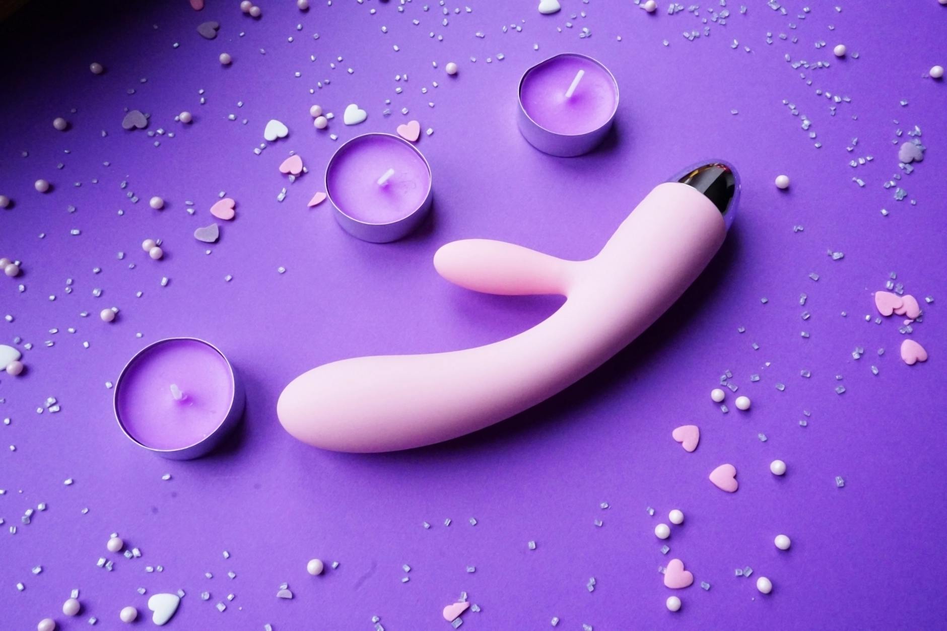 Pink lemon vibrator on purple background with heart confetti and candles for a romantic vibe.